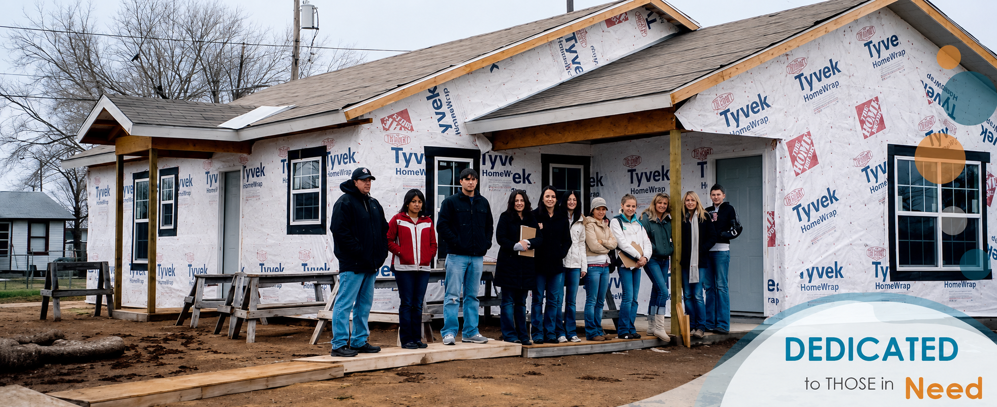 A group standing in front of a house under construction, still wrapped in housewrap
